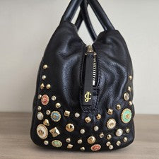 Bolso para mujer Juicy Couture negro con dijes en tono dorado tachonado herrajes